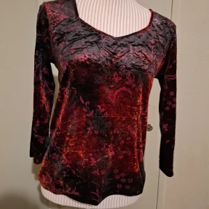 Röd sammetstopp från Kappahl - Säljer en elegant röd sammetstopp från Kappahl med v-ringning och ett vackert blommönster. Toppen har 3/4 ärmar och en glansig finish som ger en lyxig känsla. Perfekt för att lyfta vilken outfit som helst. 🌹