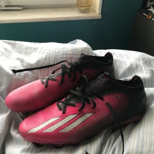  Adidas fotbollsskor (MG) - Snygga fotbollsskor i rosa och svart från Adidas med snörning och dobbar för bra grepp på planen. Skorna har en modern design med de klassiska tre ränderna i vitt på sidan. 