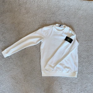 Vit tröja från Stone Island - Säljer en stilren vit tröja från Stone Island med deras ikoniska märke på ärmen. Tröjan har en klassisk rund hals och långa ärmar. Perfekt för en avslappnad och trendig look. Den är sparsamt använd