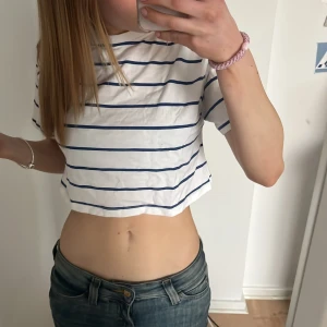 Vit och blå randig croppad topp från Kappahl - Säljer en vit och blå randig croppad topp från Kappahl. Toppen har korta ärmar och en avslappnad passform. Perfekt för en somrig look! 💙