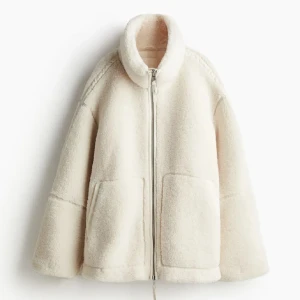 Vit teddyjacka med dragkedja - Mysig vit teddyjacka med dragkedja och stora fickor framtill. Perfekt för kyliga dagar med sin fluffiga och varma design. Jackan har en hög krage och långa ärmar för extra värme. liknar den som är från hm!