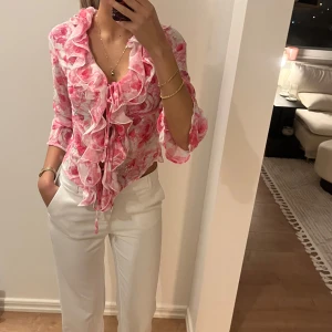 Blommig blus med volangdetaljer - Säljer en blommig blus i rosa och vit med volangdetaljer och knyt framtill. Blusen har trekvartsärmar och ett romantiskt mönster som passar perfekt för vår och sommar. Ny med lappar kvar🩷