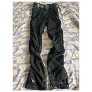 Svarta opium jeansbyxor från Japanese designer vamhrt - Snygga svarta jeansbyxor från Vamnr med vita sömmar och en stilren design. Byxorna har en klassisk femficksmodell och en bekväm passform. Perfekta för en cool och avslappnad stil.