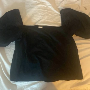 Svart topp från H&M - Säljer en svart topp från H&M med puffiga korta ärmar. Toppen har en enkel och stilren design, perfekt för olika tillfällen. Den är tillverkad i ett mjukt material som ger en bekväm passform.