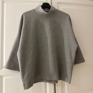 Grå oversized tröja - Säljer en stilren grå oversized tröja med hög krage och trekvartsärmar. Perfekt för en avslappnad look. Tröjan är i ett mjukt material som ger en bekväm passform.