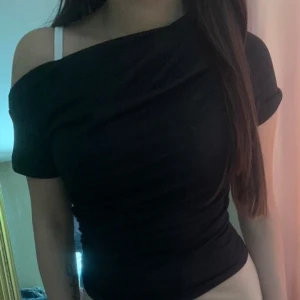 Svart offshoulder topp - Snygg svart offshoulder topp med en tight passform. Perfekt för en stilren och modern look. Toppen har en enkel design som gör den lätt att matcha med olika outfits.