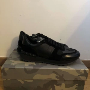 Svarta sneakers från Valentino - Snygga svarta sneakers från Valentino med ett diskret camouflage-mönster. Skorna har en klassisk snörning och är tillverkade i skinn. Perfekta för en stilren look. 