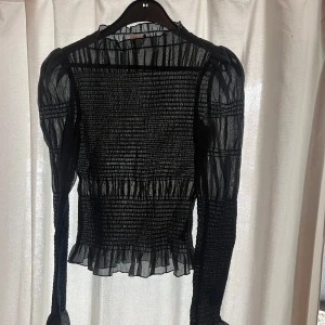 Svart/mörkgrön transparent blus - Snygg svart transparent blus med långa ärmar och volangdetaljer vid ärmslut och nederkant. Superfint skick🩷