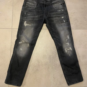 Svarta jeansbyxor från Replay med slitningar  - Snygga svarta Replay jeans med slitna detaljer för en cool look. De har en klassisk femficksdesign och en knappgylf. Perfekta för en avslappnad stil.