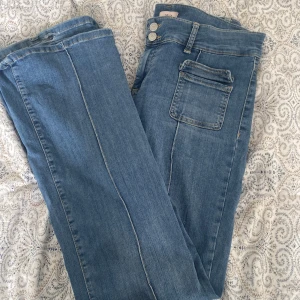 Blå bootcut jeans från Nelly - Snygga blå bootcut jeans från Nelly med låg midja och dubbla knappar. Jeansen har framträdande fickor och en linje på som design. Lite slitna på slutet av byxorna. Original pris 699 men säljer för 450kr.