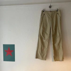 Beige byxor med dragkedja - Snygga beige byxor med dragkedja vid fickorna. De har en flared/baggy passform och är perfekta för en avslappnad stil. Byxorna är tillverkade i ett lätt material som ger en bekväm känsla. Y2k