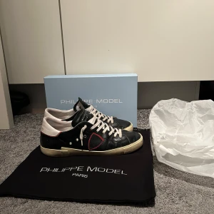 Philippe Model  - Snygga svarta sneakers från Philippe Model med vita och röda detaljer. Skorna har snörning och en klassisk design som passar perfekt för en stilren look. De kommer med originalförpackning och påse. Bra skick, 8,5/10… Nypris 3600