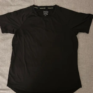 Svart t-shirt från Xside Active - Säljer en svart t-shirt från Xside Active. Perfekt för träning med sin bekväma passform och korta ärmar. Materialet är lätt och andas bra, vilket gör den idealisk för aktiva dagar.