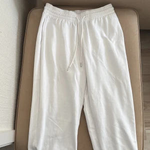 Vita mjukisbyxor från H&M - Säljer ett par vita mjukisbyxor från H&M. Byxorna har en elastisk midja med snörning och ribbade muddar vid bensluten. Perfekta för en avslappnad stil.