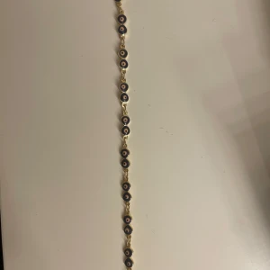 Armband med evil eye 🧿  - Snyggt armband med evil eye i blått, vitt och guld. Armbandet har flera små runda hängen med ett öga i mitten, kopplade med guldfärgade länkar. Perfekt för att ge en unik touch till din stil. Köpte i Grekland för 200kr💕