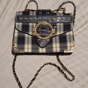 Liten rutig handväska  - Fin liten handväska med ett rutigt mönster och guldiga detaljer. Säljer då jag aldrig använder den. Mycket fint skick, har en liten defekt som syns på bild 5. Tar swish, köparen föreslår pris 🍀