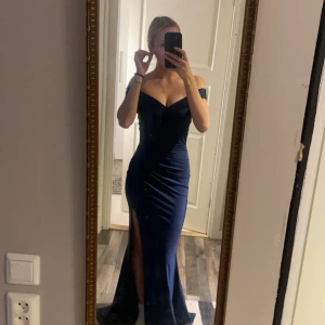 Marinblå långklänning - Elegant marinblå långklänning med offshoulder-design och en stilren slits framtill. Perfekt för en festlig kväll med en figurnära passform som framhäver silhuetten. PRIS GÅR ATT DISKUTERA!