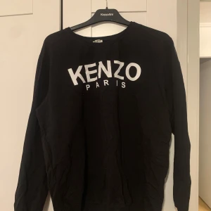 Svart långärmad tröja från Kenzo - Säljer en svart långärmad tröja från Kenzo med vit logotyp på framsidan. Perfekt för en stilren och avslappnad look. Tröjan har en klassisk passform och är tillverkad i ett mjukt material. I storlek 4XL men skulle säga att den är mer som en XS-S