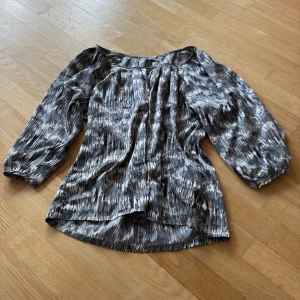 Mönstrad blus i svart och grått - Säljer en snygg blus med ett abstrakt mönster i svart och grått. Blusen har trekvartsärmar och en lös passform, perfekt för en stilren look.