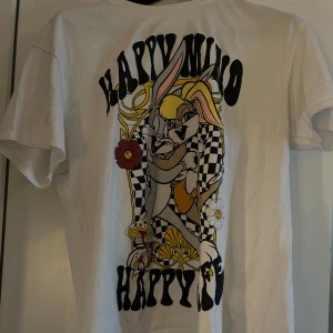 Vit t-shirt med tryck - Säljer en vit t-shirt med ett färgglatt tryck av tecknade figurer och texten 'Happy Mind'. T-shirten har korta ärmar och en rund halsringning. 