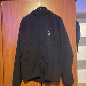 Haglöfs jacka - Säljer en svart jacka från Haglöfs med dragkedja och huva. Jackan har långa ärmar och två fickor med dragkedjor framtill. Perfekt för kyligare dagar. Modellen är 187cm och väger 85kg. Det står XL men passar L