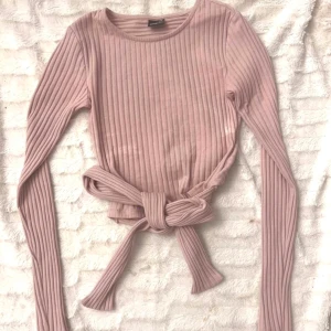 Rosa ribbad tröja med knyt - Säljer en söt rosa ribbad tröja med långa ärmar och knytning i midjan. Perfekt för en stilren och bekväm look. . 🌸 Storlek XXS / 32. Använd en gång innan den blev för liten för mig. Obs inga fläckar utan kameran reflekterade ljuset konstigt
