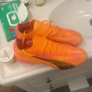 Orange och rosa fotbollsskor - Säljer ett par riktigt snygga fotbollsskor i orange och rosa. De har en cool design med svarta detaljer på sidan och är perfekta för att sticka ut på planen. Skorna har snörning och är i nyskick. Perfekta för fotbollsträning eller match!