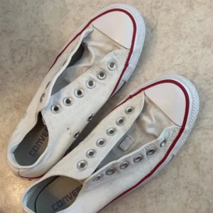 Vita Converse All Star sneakers - Säljer ett par vita Converse All Star sneakers i storlek 37,5 Skorna är i bra skick med några tecken på användning. De har den klassiska designen med röd och blå rand på sulan och är tillverkade i canvasmaterial. Perfekta för vardagsbruk och passar till det mesta!