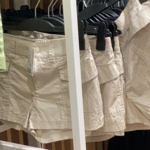 Shorts - Säljer dessa trendiga beiga cargoshortsen i stl 34. Jag säljer dem eftersom dem inte har kommit till användning. Jag skulle säga att dem sitter low/mid-waist på mig men jag brukar vika ned dem. Nypris är 200kr. 