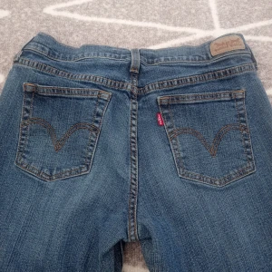Blå jeans från Levi's - Säljer ett par klassiska blå jeans från Levi's. De är i bra skick och har en snygg, tidlös design med fem fickor och knappgylf. Perfekta för vardagsbruk och kan matchas med nästan vad som helst+ ger också ett par gratis smycken. Passar med sneakers.