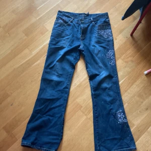 Bootcutjeans med blommbroderi  - Bootcutjeans med blått blombroderi och gemstones vet inte riktigt märket eftersom att jag köpte de secondhand och lappen är svår att tyda. Pris kan diskuteras. Kolla på mitt konto för liknande jeans