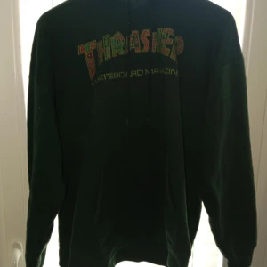 Grön Thrasher hoodie - Säljer en grön Thrasher hoodie i storlek M. Den är perfekt för skateboarding eller bara för att chilla. Hoodien har en stor Thrasher-logga på framsidan i färgglada bokstäver. Den är långärmad och gjord av bomull, vilket gör den både bekväm och hållbar. Perfekt för höst och vinter!
