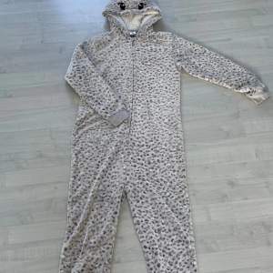 Säljer en supermysig grå leopardmönstrad onesie från Lindex. Den har en söt huva med ögon och öron, och är gjord av mjuk fleece. Perfekt för kalla dagar när du bara vill mysa hemma. Den har en dragkedja framtill och är i storlek 170, vilket passar för 14+ år. Använd några gånger men i bra skick!