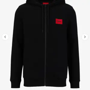 Säljer en stilren svart hoodie från Hugo med en röd logga på bröstet. Den har dragkedja och en skön huva med snören. Perfekt för både vardag och chill. Passar till allt och är superbekväm! 