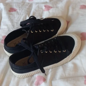 Svarta sneakers med vit sula - Säljer ett par snygga svarta sneakers med vit sula och snörning. Perfekta för vardagsbruk och ger en stilren look. De är i bra skick och passar till de flesta outfits.