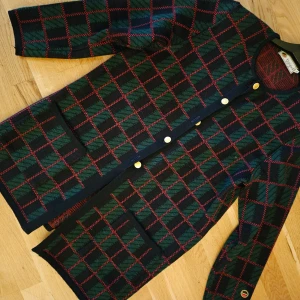 Rutig kavaj med guldknappar - Säljer en snygg rutig längre kofta i grönt och rött med guldknappar. Den har långa ärmar och två fickor fram. Perfekt för höst och vinter, och funkar både till vardags och fest. Koftan  är i mycket bra skick och ger en klassisk look. Lång kvalitetskofta i ull från Busnel. Kommer hålla i 100 år. Svart-grön-röd. Perfekt till jul, middag och vardag.