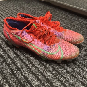Röda fotbollsskor från Nike - Säljer ett par röda Nike fotbollsskor i bra skick. De har en cool design med gröna detaljer och snörning. Perfekta för fotbollsträning eller match. Skorna har en tight passform och är gjorda för att ge bra grepp på planen.