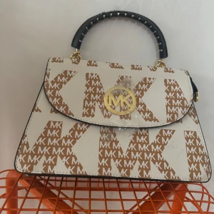 Michael Kors handväska med logotypmönster - Snygg handväska från Michael Kors med deras ikoniska logotypmönster i brunt och vitt. Väskan har ett svart handtag och en praktisk dragkedja. Perfekt för både vardag och fest!