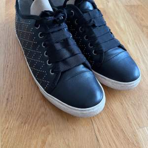 Säljer ett par svarta sneakers från Lanvin i bra skick. Skorna har snygga detaljer med små pärlor på sidorna och breda svarta snören. De har en vit sula med Lanvin-logga undertill. Perfekta för både vardag och fest! Storleken visar 38 men har själv 40 och de sitter bra