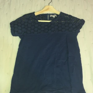 Mörkblåthsirt med detaljer - Säljer en elegant mörkblå tröja med vackra spetsdetaljer upptill. Tröjan har korta ärmar och en normal passform, perfekt för både vardag och festliga tillfällen. Materialet känns mjukt och bekvämt mot huden. Passar bra till både sommar och höst.