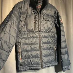 Mörkblå quiltad jacka från Canada Snow.  - Säljer en mörkblå quiltad jacka från Canada Snow. Den har en dragkedja framtill och flera praktiska fickor med dragkedjor. Jackan är perfekt för höst och vår.  Det finns en liten skada på baksidan, men annars i bra skick.