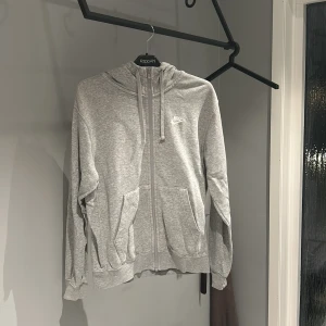 Grå hoodie från Nike - Säljer en grå hoodie från Nike i mycket bra skick. Den har en dragkedja framtill och en justerbar huva med snören. Perfekt för både träning och vardag. Supermjuk och bekväm att ha på sig! 🩶