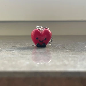 Nyckelring med rött hjärta - Söt nyckelring med ett rött hjärta som har ett glatt ansikte och små svarta fötter. Perfekt för att ge lite personlighet till dina nycklar eller väskor. Hängaren är i metall och lätt att fästa. Hjärtdesignen är både rolig och charmig, perfekt som en liten present eller för att lysa upp din dag! 💖