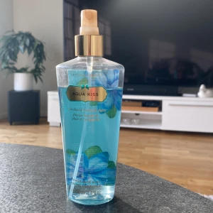Aqua Kiss Fragrance Mist från Victoria's Secret - Säljer en fräsch och blommig Aqua Kiss Fragrance Mist från Victoria's Secret. Den har en härlig doft av regnkyssad fresia och tusensköna. Flaskan är genomskinlig med blå vätska och dekorerad med blå blommor. Perfekt för en uppfriskande känsla!
