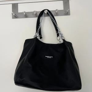 Svart axelväska med kedjedetaljer - Snygg svart väska som jag ej vet vart den är ifrån men aldrig använd därav i ett mycket bra skick 