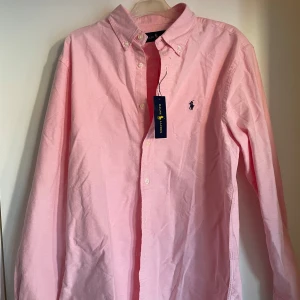 Rosa skjorta från Ralph Lauren - Säljer en snygg rosa skjorta från Ralph Lauren i storlek M. Skjortan är i nytt skick med knappar och en klassisk krage. Perfekt för både vardag och fest! 💖