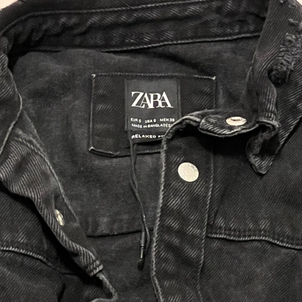 Säljer en svart jeansskjorta från Zara i avslappnad stil. Skjortan har slitna detaljer och knappar framtill. Perfekt för en cool och avslappnad look. Passar bra till både vardag säljs för 80. Skjortor.