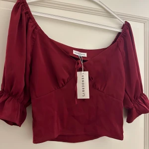 Vinröd topp från Venderbys - Snygg vinröd topp från Venderbys med korta puffärmar och en söt knytning framtill❤️Perfekt för en kväll ute eller en festlig tillställning. Toppen har en v-ringad design och är croppad för en trendig look.