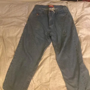 Baggy jeans från Butter - Säljer ett par baggy jeans från Butter i blå denim. De har en broderad detalj på fickan. Perfekta för en avslappnad stil med elastisk midja och snörning.