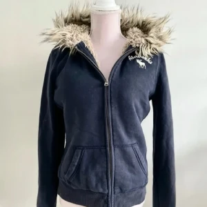 Abercrombie & Fitch - IMTRESSEKOLL 🫶🏼 Funderar på att sälja min super snygga 2000s mörkblåa zip up hoodie från Abercrombie & Fitch med fuskpäls på huvan och inuti, då jag är osäker om jag tycker om hur den sitter på mig! Den har dragkedja framtill och långa ärmar. Storlek M men skulle säga att den är mer som XS-S (mindre i storleken) Perfekt för kyliga dagar 💕 Ge prisförslag!